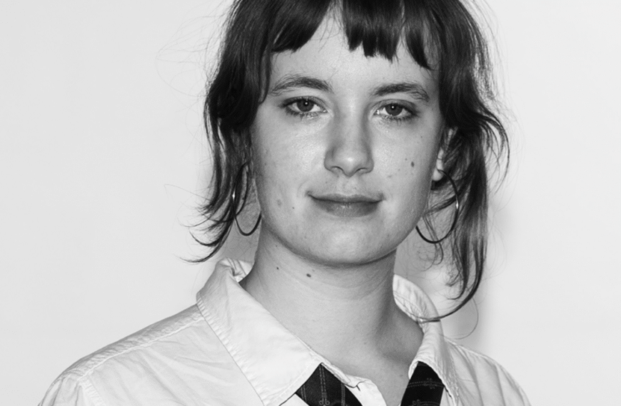 Linnea Sundberg har en vit skjorta med en svart slips, och brunt hår.